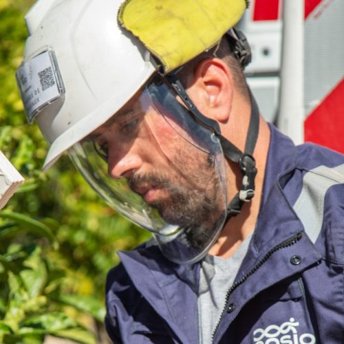 Technicien ENSIO en combinaison bleue et casque avec visière de protection raccordant un câble électrique lors d'un branchement sur le réseau